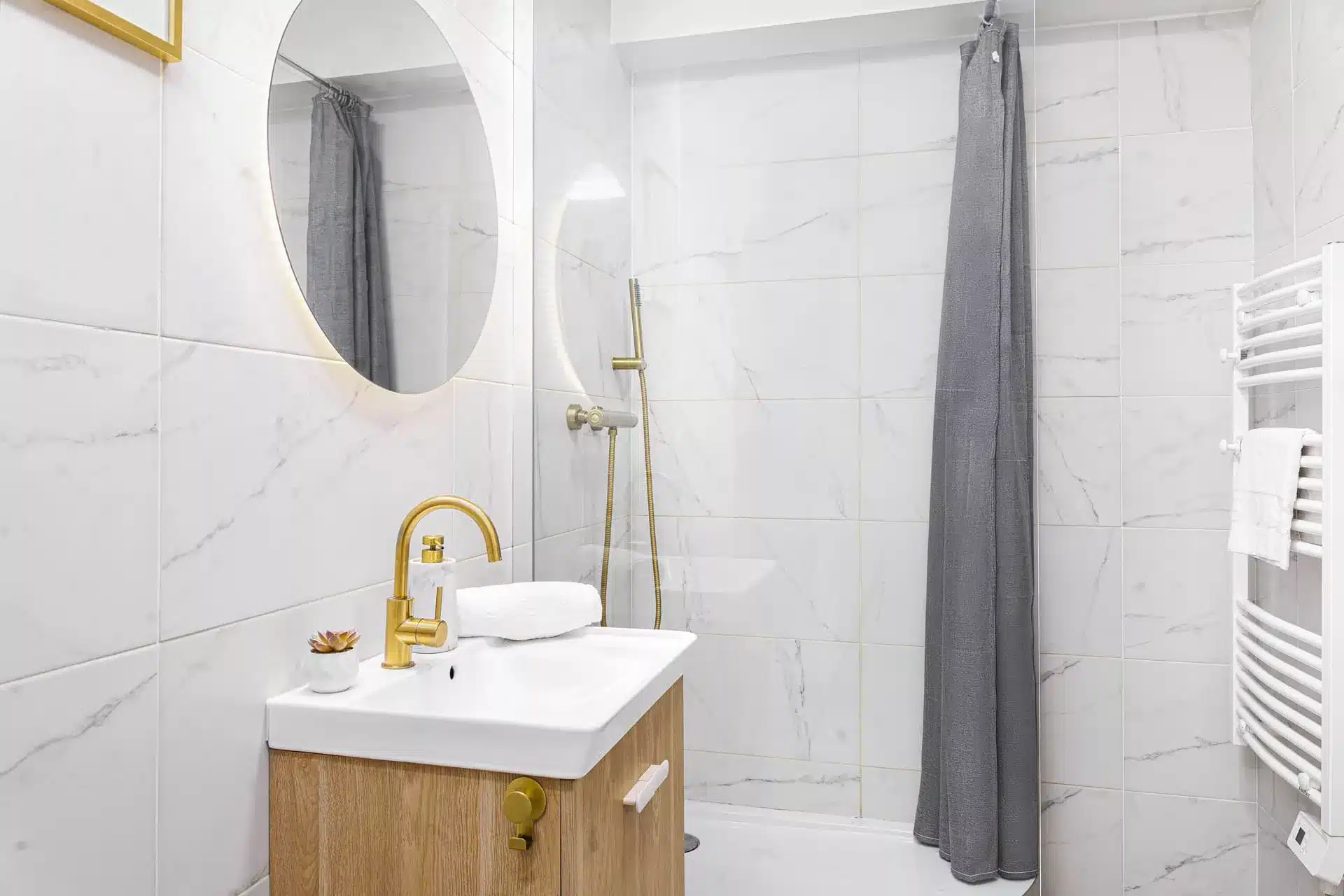 Image immobilière professionnelle - salle de bain carrelage marbre blanc avec robinetterie dorée et miroir rond rétroéclairé – Évry-Courcouronnes 91000